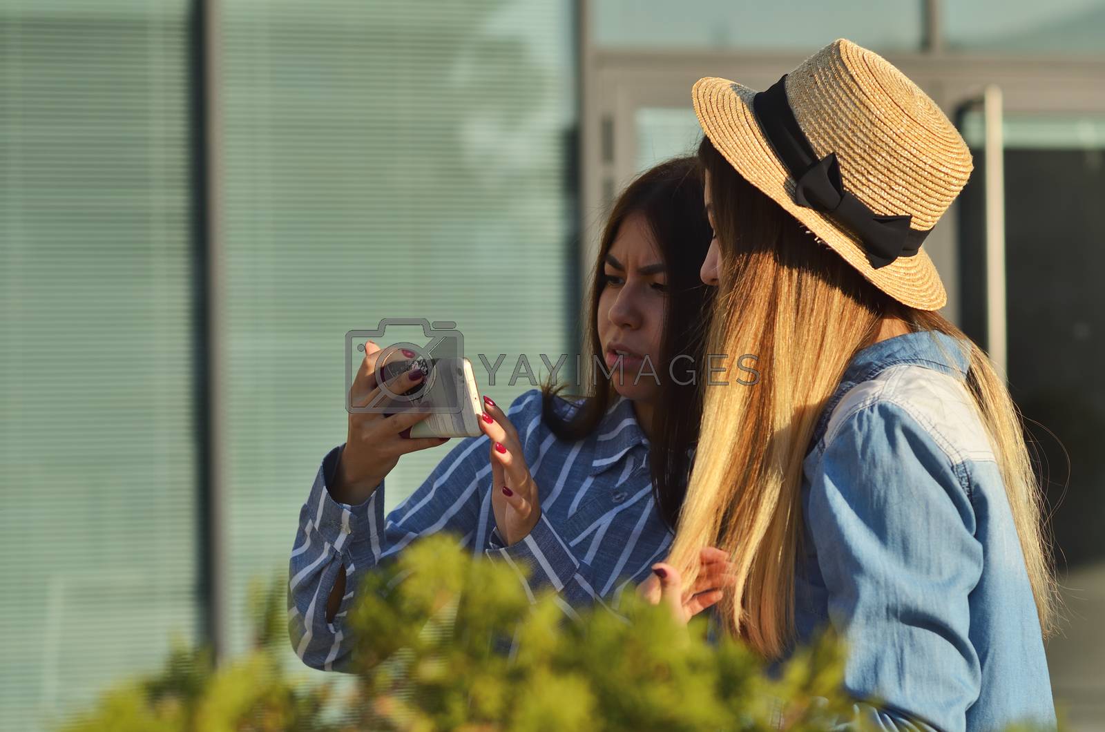 Royalty free image of Two young girls communicate in social networks by phone walking on the street on a Sunny day by xzgorik