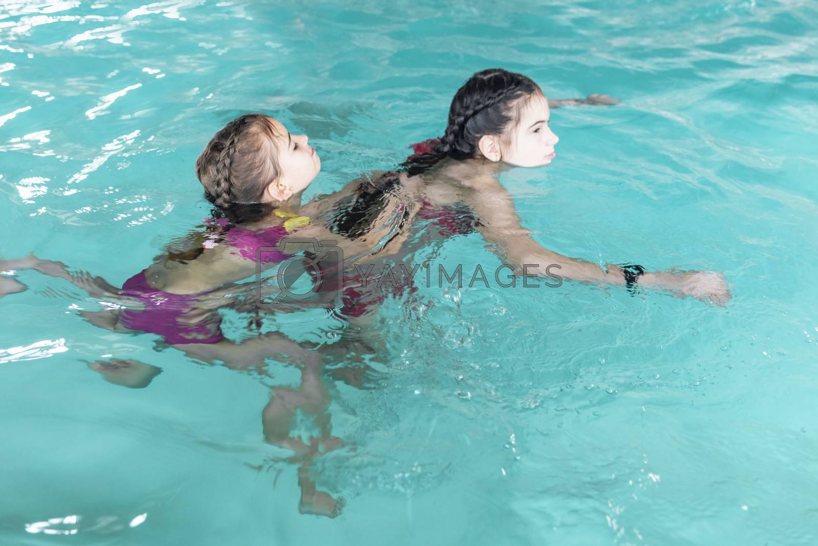 Royalty free image of Two girls swim in the pool. Two sisters in the pool. Two happy girls play in the pool.Beautiful girls swim and having fun in water.Active holiday. by nkooume