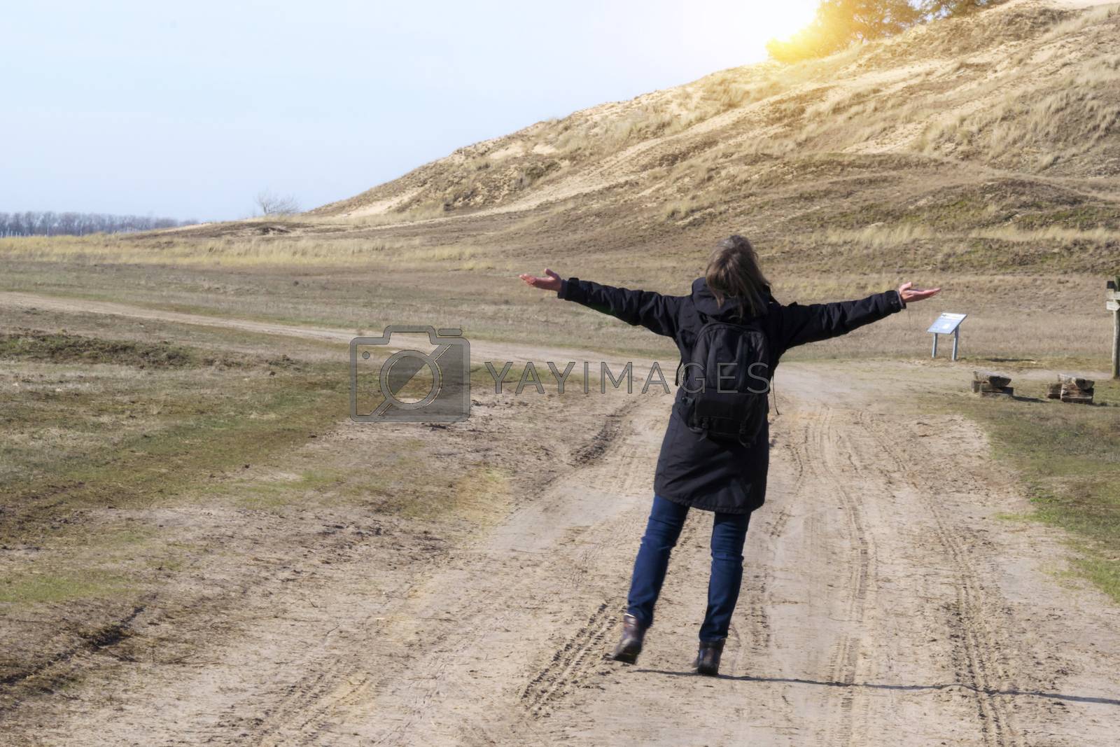 Royalty free image of Caucasian woman in black coat arms raised on empty road towards sunset by Fr@nk