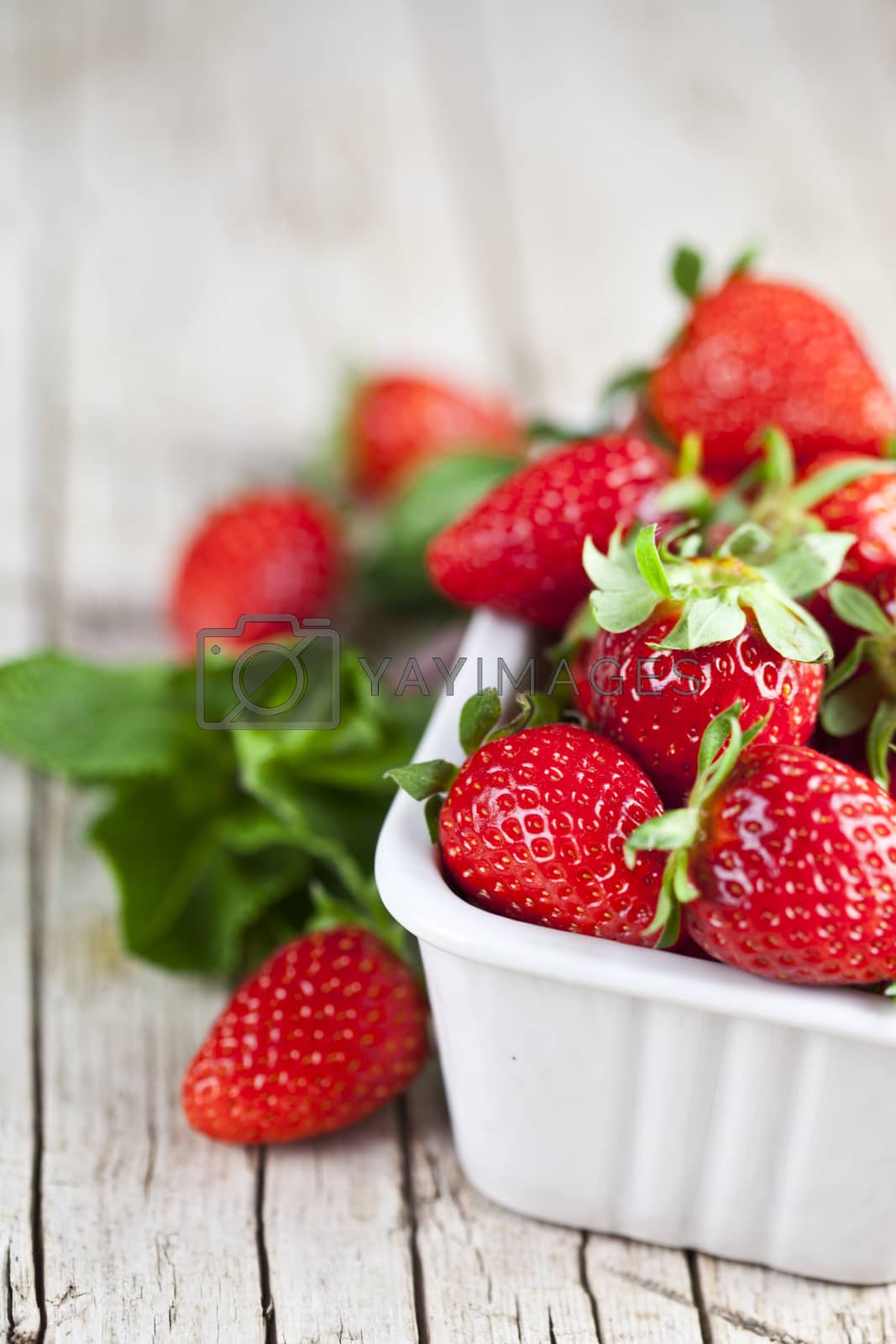 Royalty free image of Fresh red strawberries in white bowl and mint leaves on rustic w by marylooo