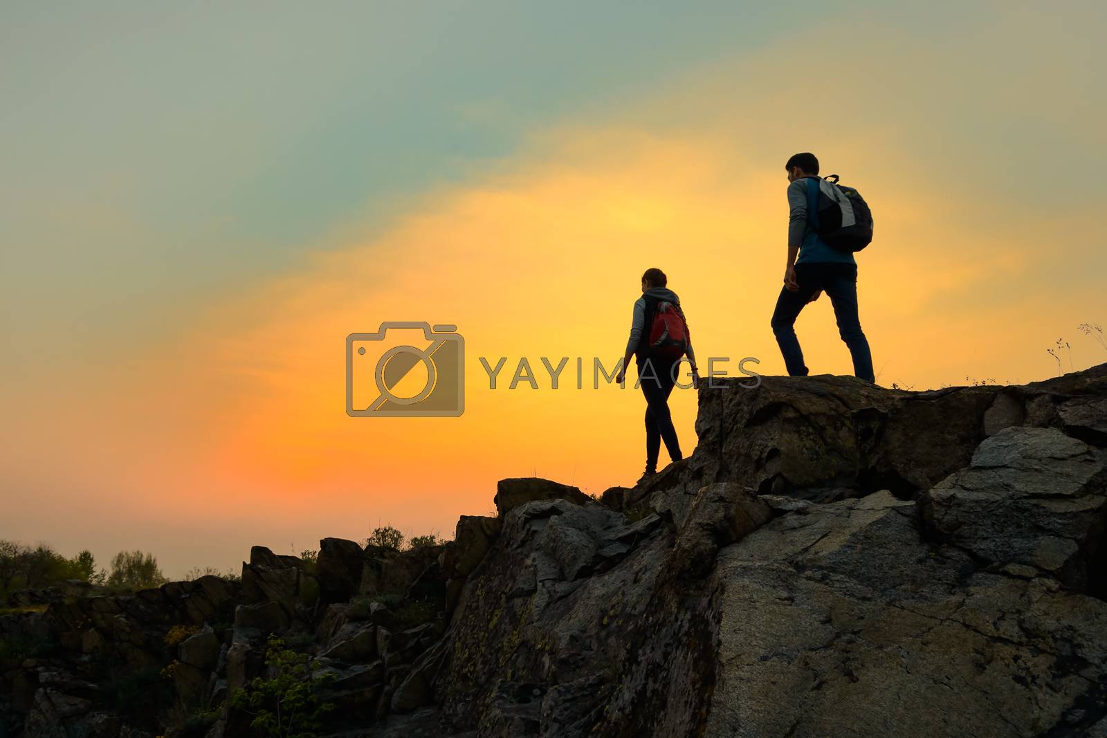 Royalty free image of Young Happy Travelers Hiking with Backpacks on the Rocky Trail at Summer Sunset. Family Travel and Adventure Concept. by maxpro