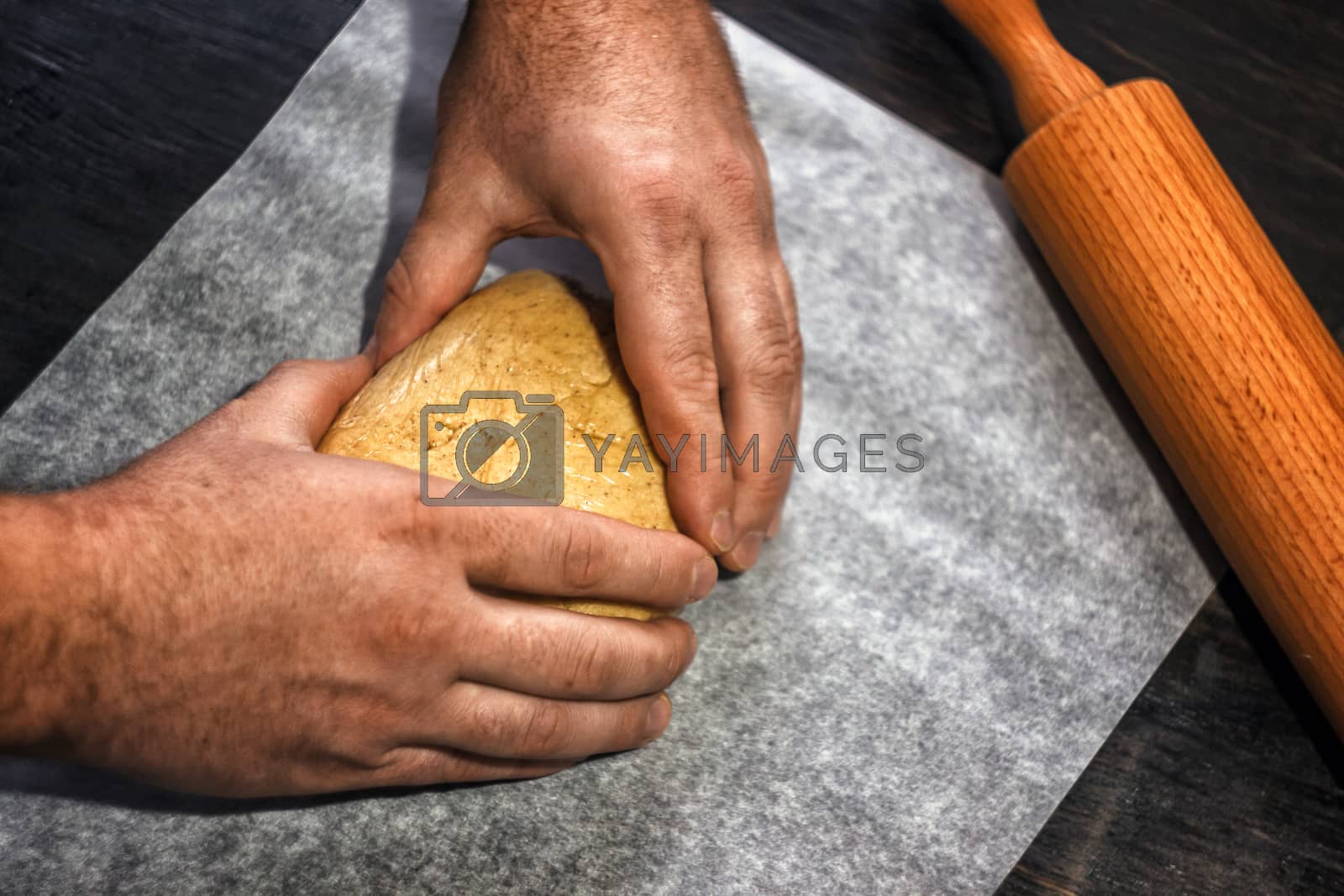 Royalty free image of man's hands knead the dough in retro style on a dark background by Tanacha