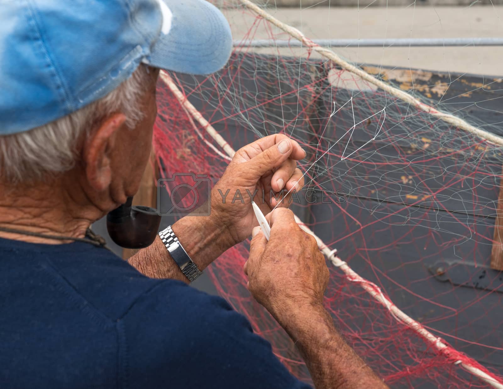 Royalty free image of Senior fisherman repairs fishing net by Robertobinetti70