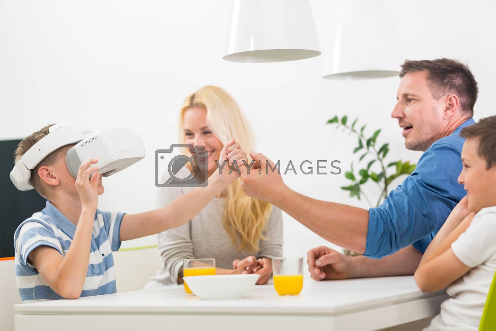 Royalty free image of Happy caucasian family at home at dinning table, having fun playing games using virtual reality headset by kasto