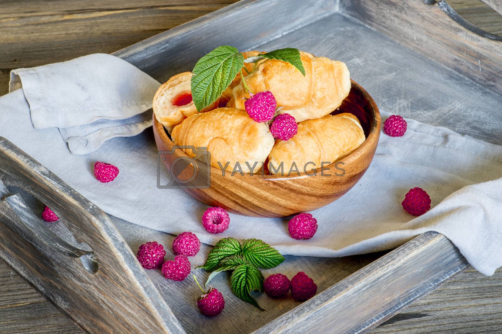 Royalty free image of Croissants with raspberries on a wooden tray. The concept of a wholesome breakfast. by AlisLuch