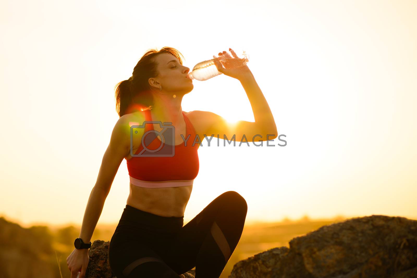 Royalty free image of Woman Resting and Drinking Water after Running Outdoor. Workout at Hot Summer Sunset. Sport and Healthy Active Lifesyle. by maxpro