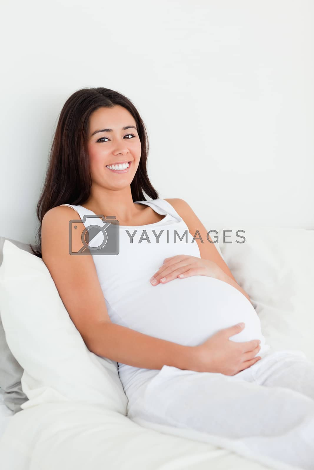Royalty free image of Frontal view of a pretty pregnant woman touching her belly while lying on a bed by Wavebreakmedia