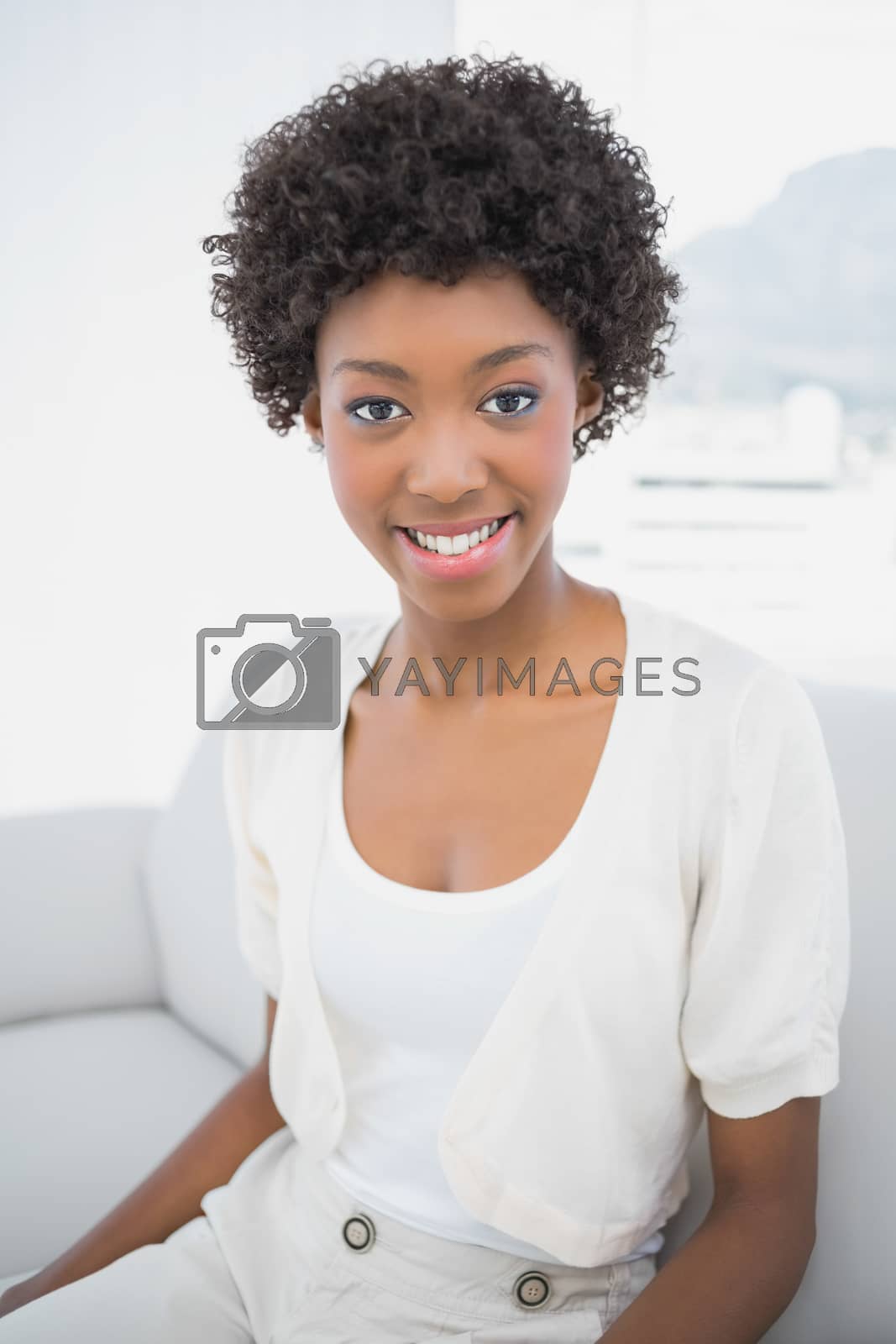 Royalty free image of Smiling pretty brunette sitting on cosy sofa by Wavebreakmedia