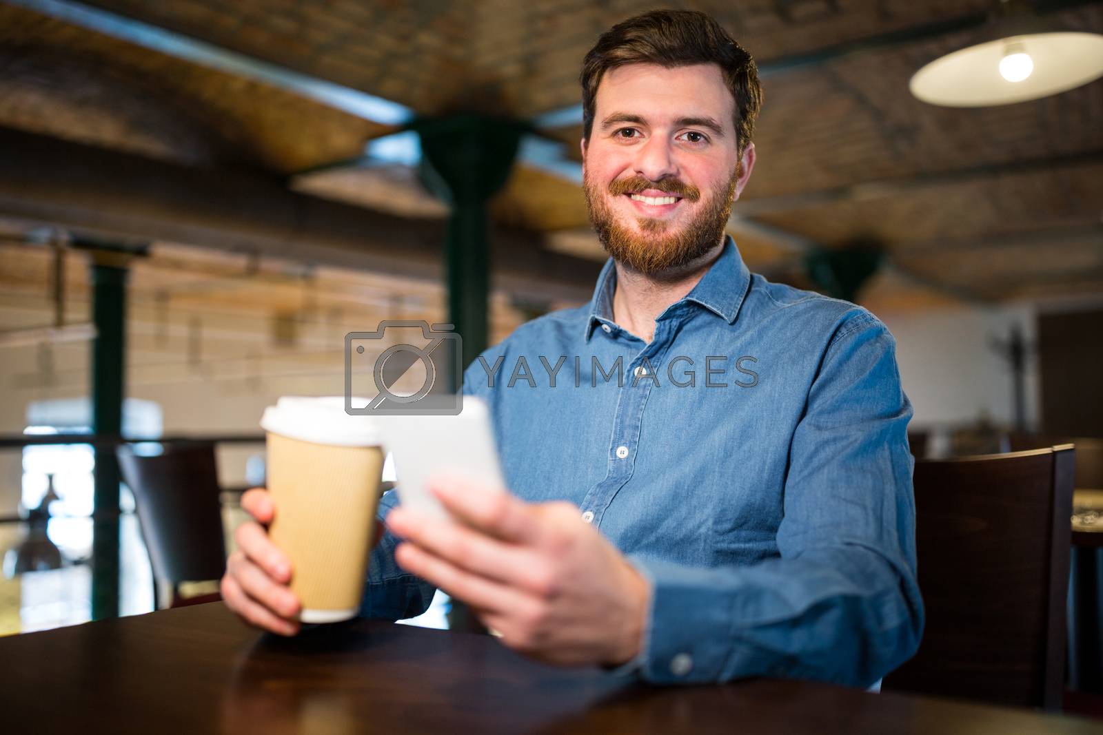 Royalty free image of Man holding disposable coffee cup and mobile phone by Wavebreakmedia