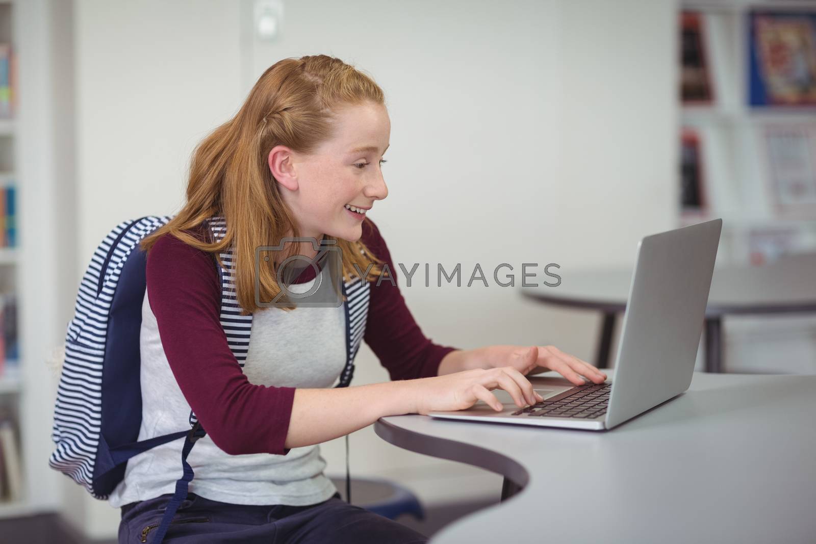 Royalty free image of Happy schoolgirl with schoolbag using laptop in library by Wavebreakmedia