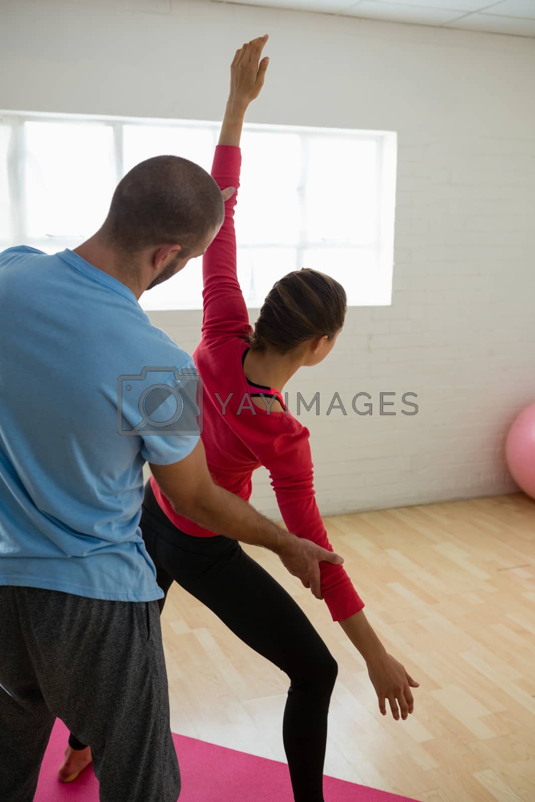 Royalty free image of Yoga instructor assisting student in exercising at health club by Wavebreakmedia