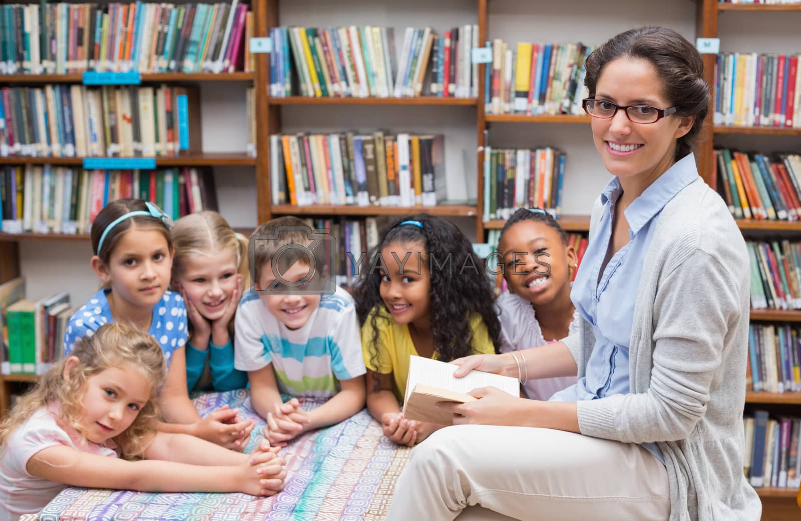 Royalty free image of Cute pupils and teacher reading in library by Wavebreakmedia