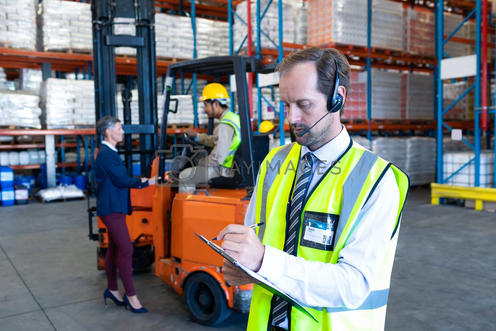 Royalty free image of Male supervisor with headset writing on clipboard in warehouse by Wavebreakmedia