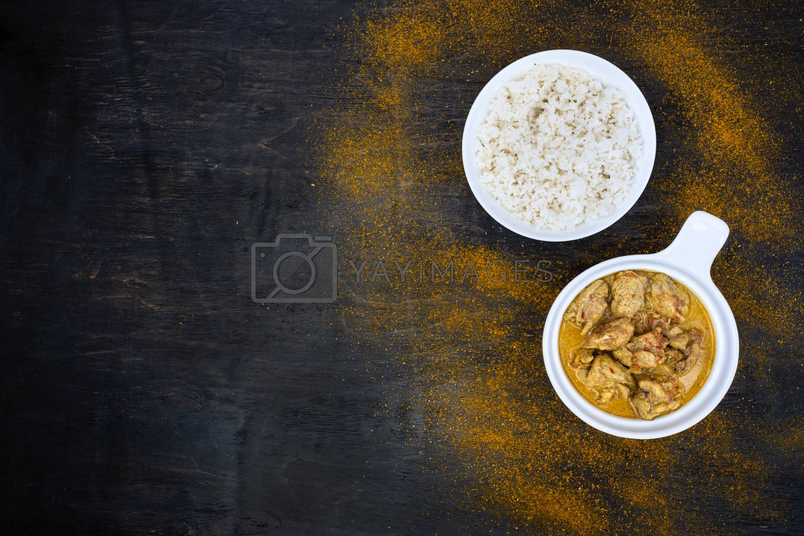 Royalty free image of Orange spicy chicken curry and rice in simple white plates on a dark background. Around hot pepper, lemon, curry powder. Indian traditional cuisine. Flat lay. Top view, copy space. by Tanacha