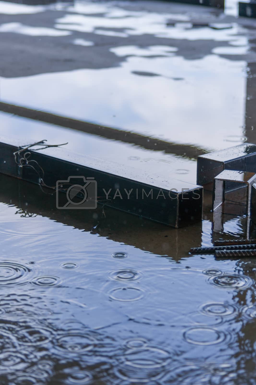 Royalty free image of Big square metal pipes parts under rain on construction with sky in reflection. by alexsdriver