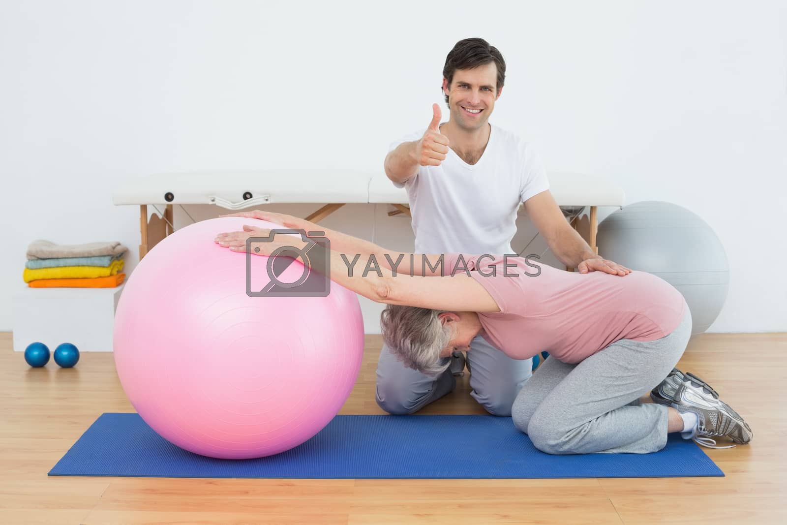 Royalty free image of Therapist gesturing thumbs up by senior woman with yoga ball by Wavebreakmedia