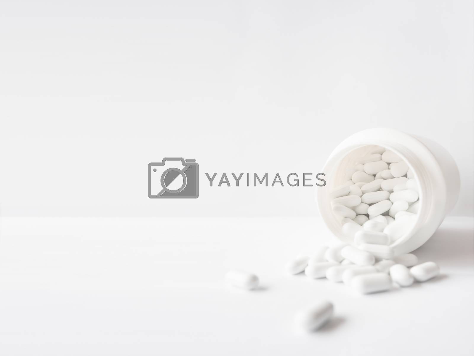 Royalty free image of White pills spilled out of a plastic jar. Medicine capsules on w by aksenovko