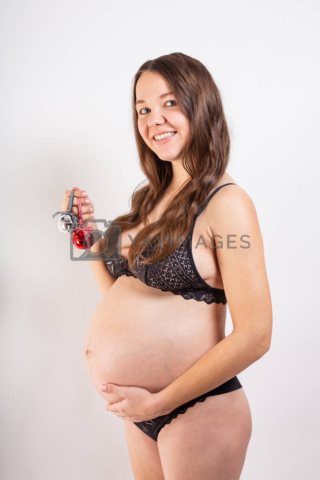 Royalty free image of Beautiful pregnant girl on a white background holds Christmas toys in her hands. by Vassiliy