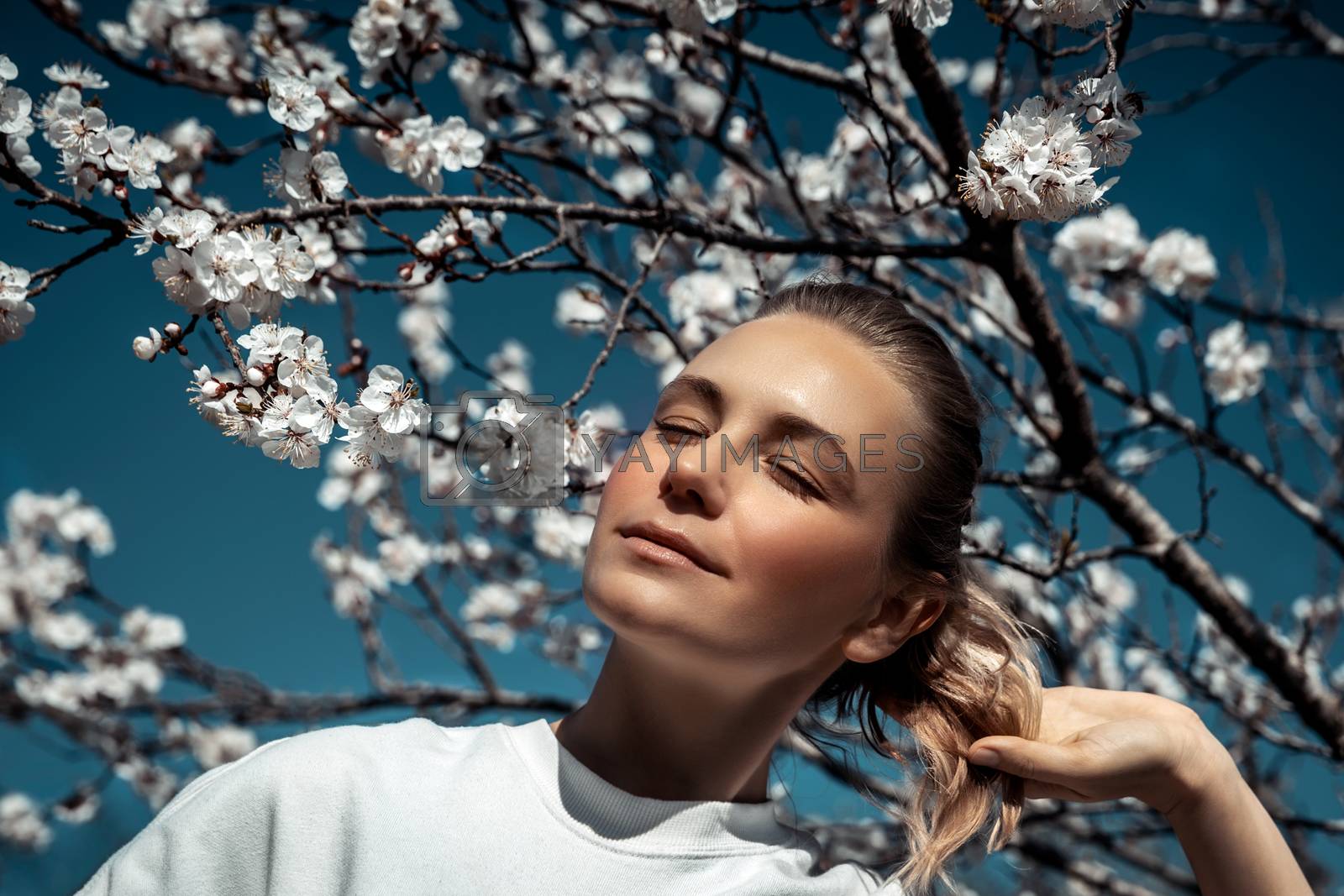 Fashion portrait of a nice female with closed eyes of pleasure enjoying beauty and freshness of spring nature, spending time in blooming garden, weekend in countryside
