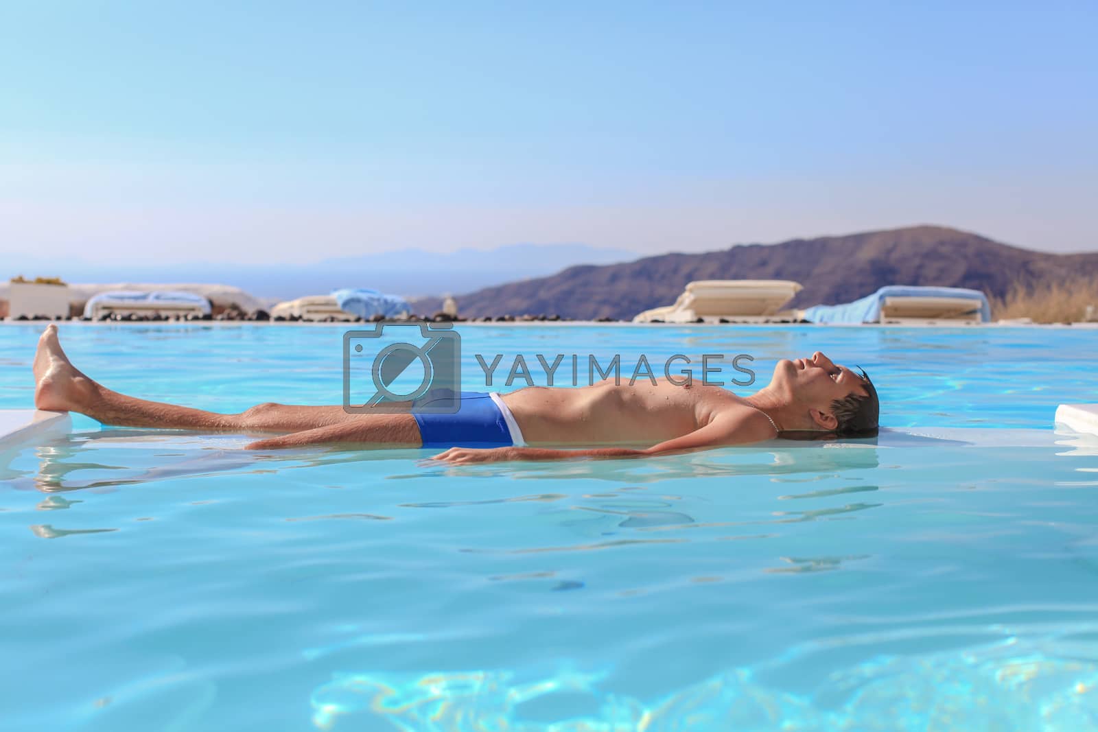 Royalty free image of Young man in infinity swimming pool in Santorini, Greece by travnikovstudio
