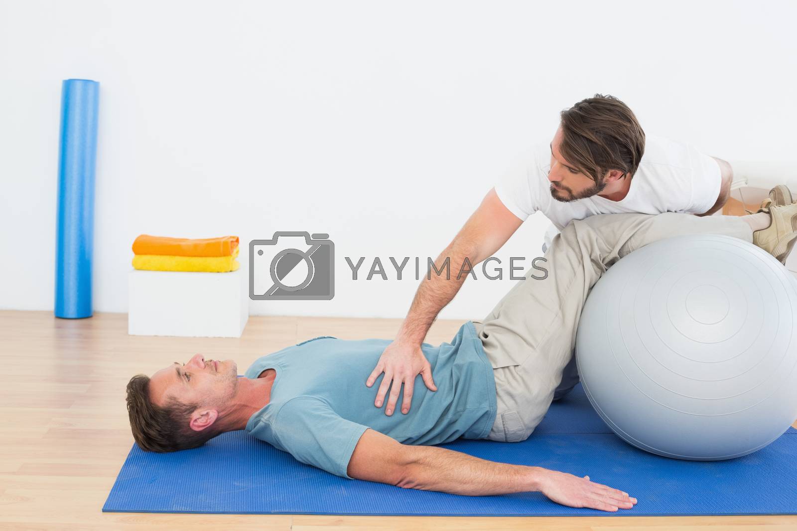 Royalty free image of Physical therapist assisting young man with yoga ball by Wavebreakmedia