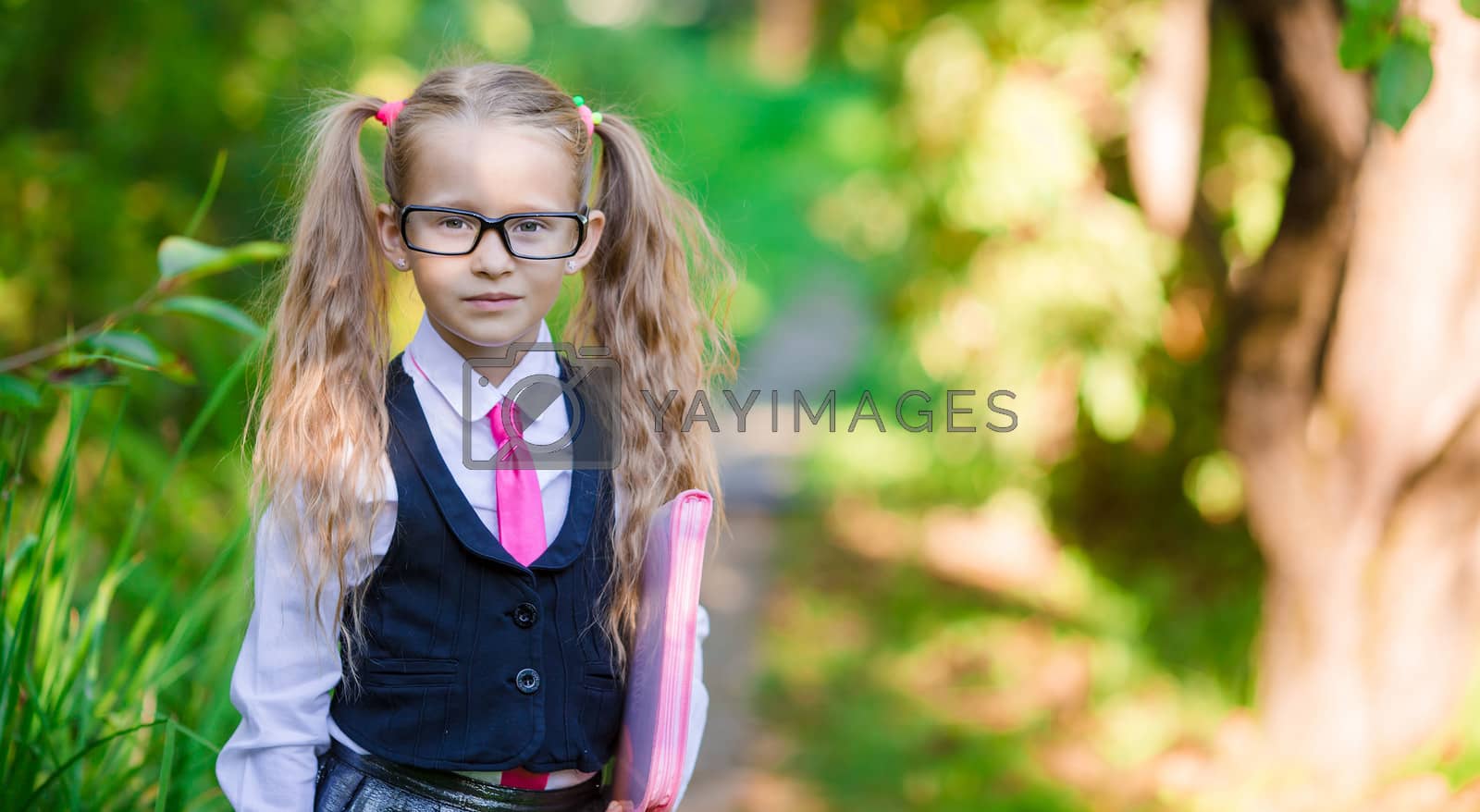 Royalty free image of Portrait of adorable little school girl with notes in glasses outdoor going to school by travnikovstudio