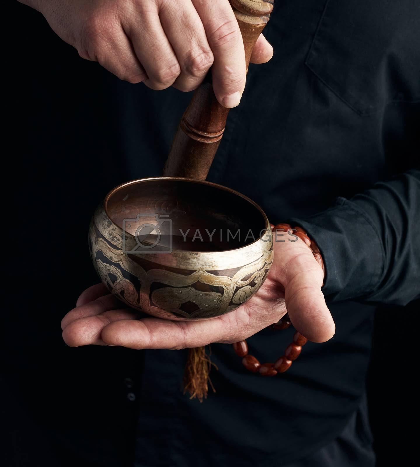 Royalty free image of man in a black shirt rotates a wooden stick around a copper Tibe by ndanko