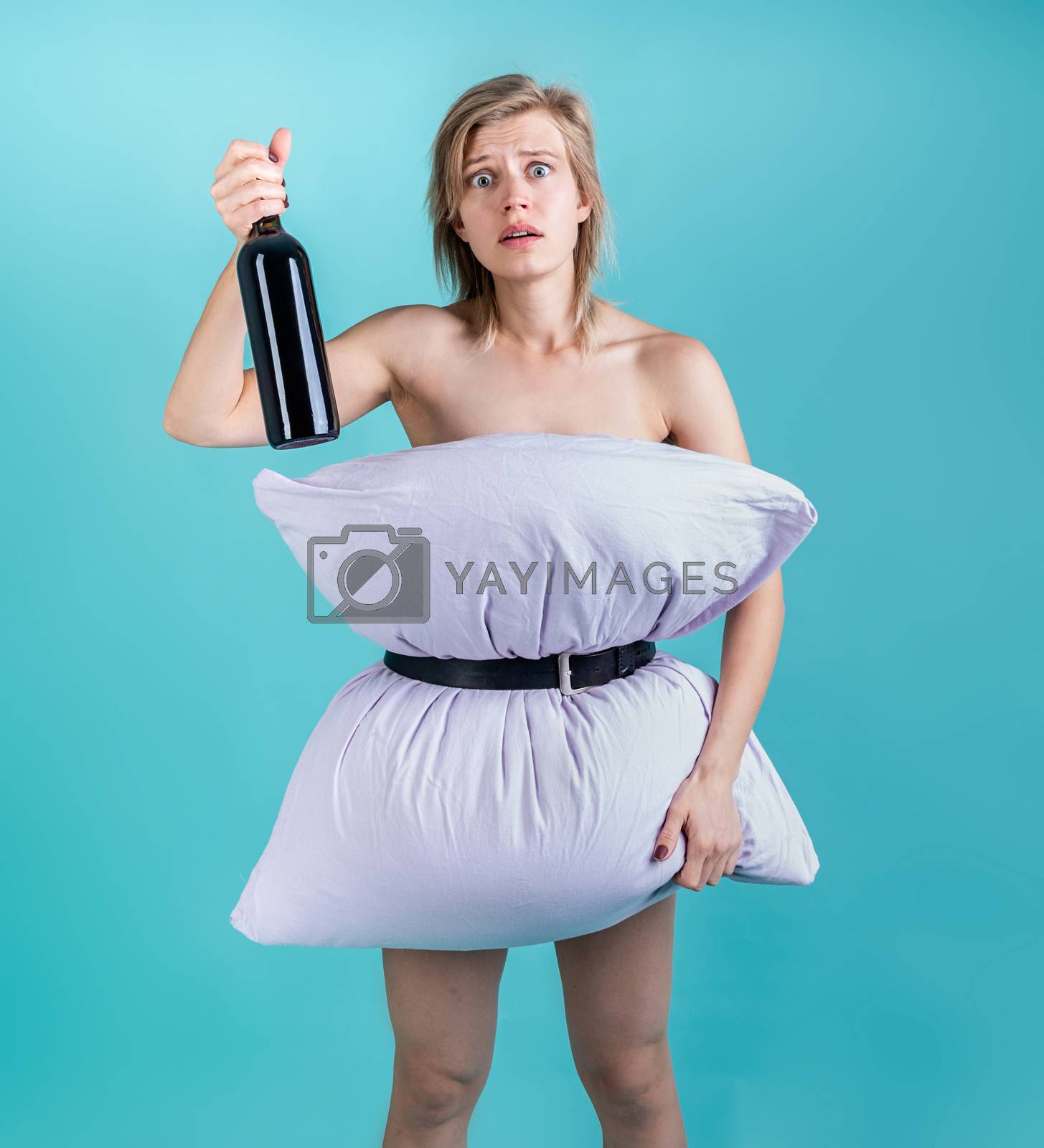 Royalty free image of Desperate woman in pillowdress holding a wine bottle isolated on blue background by Desperada
