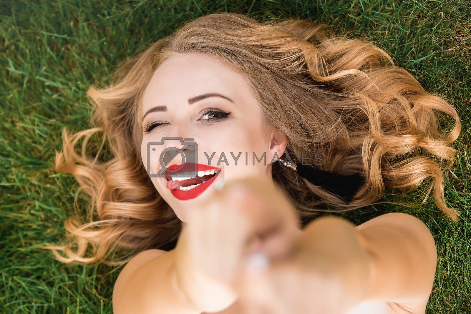 Royalty free image of Caucasian pretty woman with curly black hair lying on the grass in the park. Smile and calm. portrait of Caucasian woman with blond hair spending day at nature by Nickstock