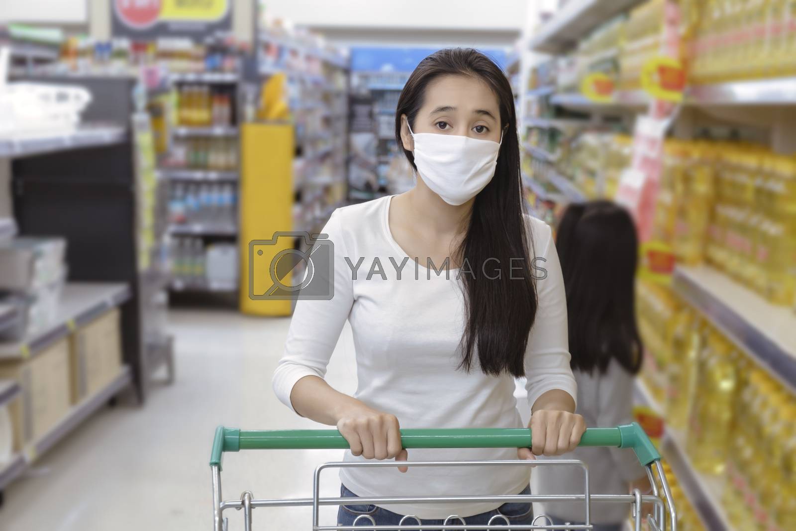 Royalty free image of Asian woman wear face mask push shopping cart in suppermarket de by Satrinekarn