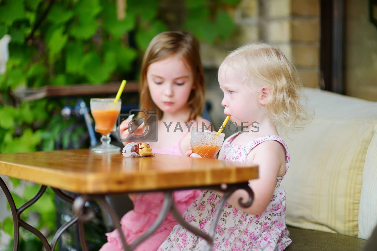 Royalty free image of Two sisters drinking juice and eating pastries by maximkabb