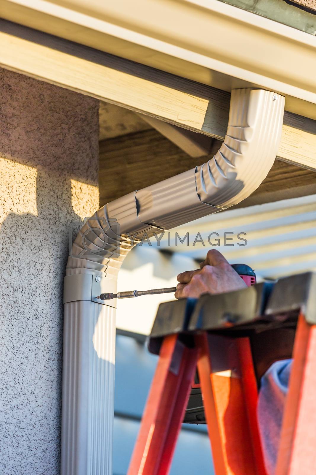 Royalty free image of Worker Attaching Aluminum Rain Gutter and Down Spout to Fascia of House. by Feverpitched