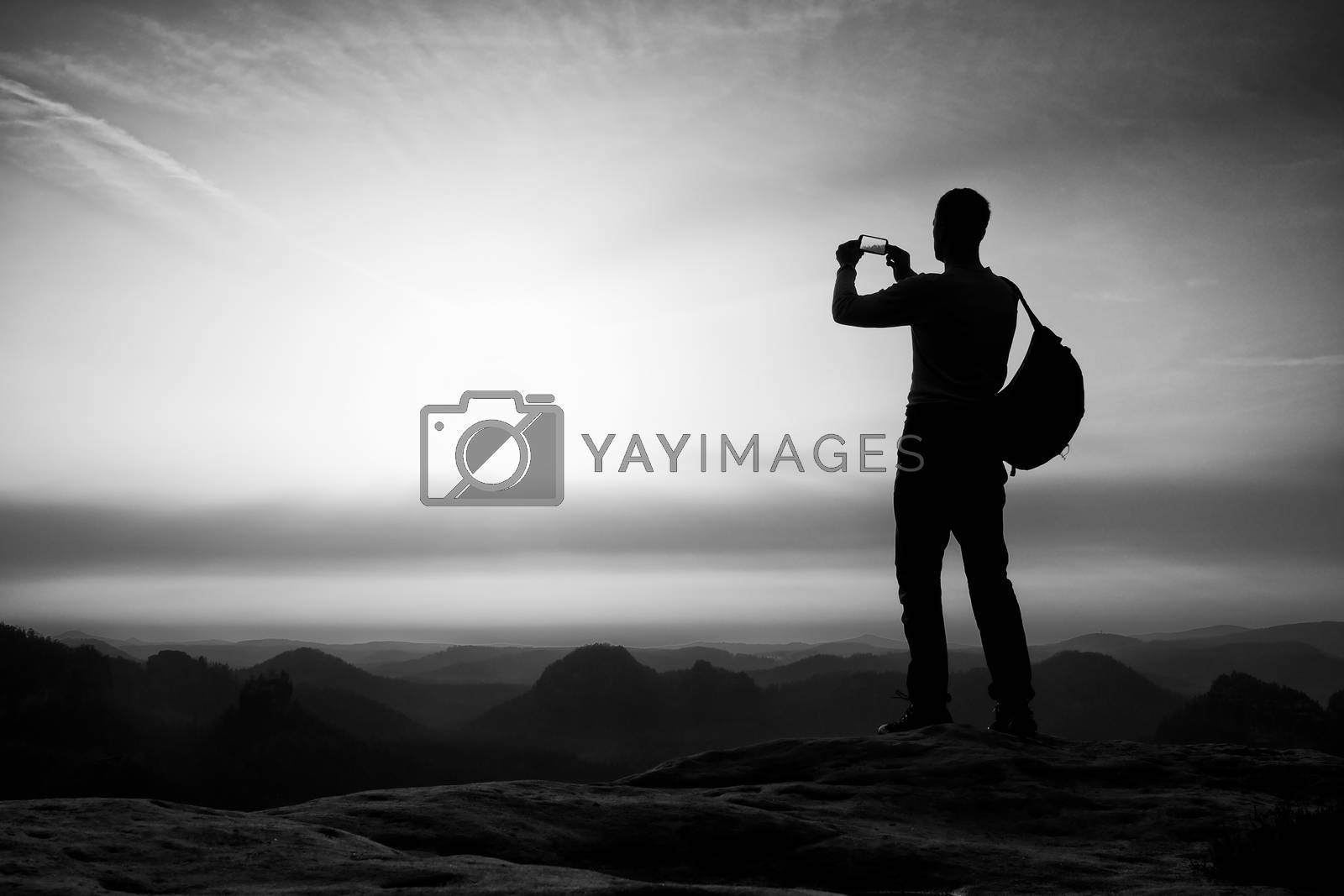Royalty free image of Tourist with backpack takes photos with smartphone on peak. Orange daybreak by rdonar2