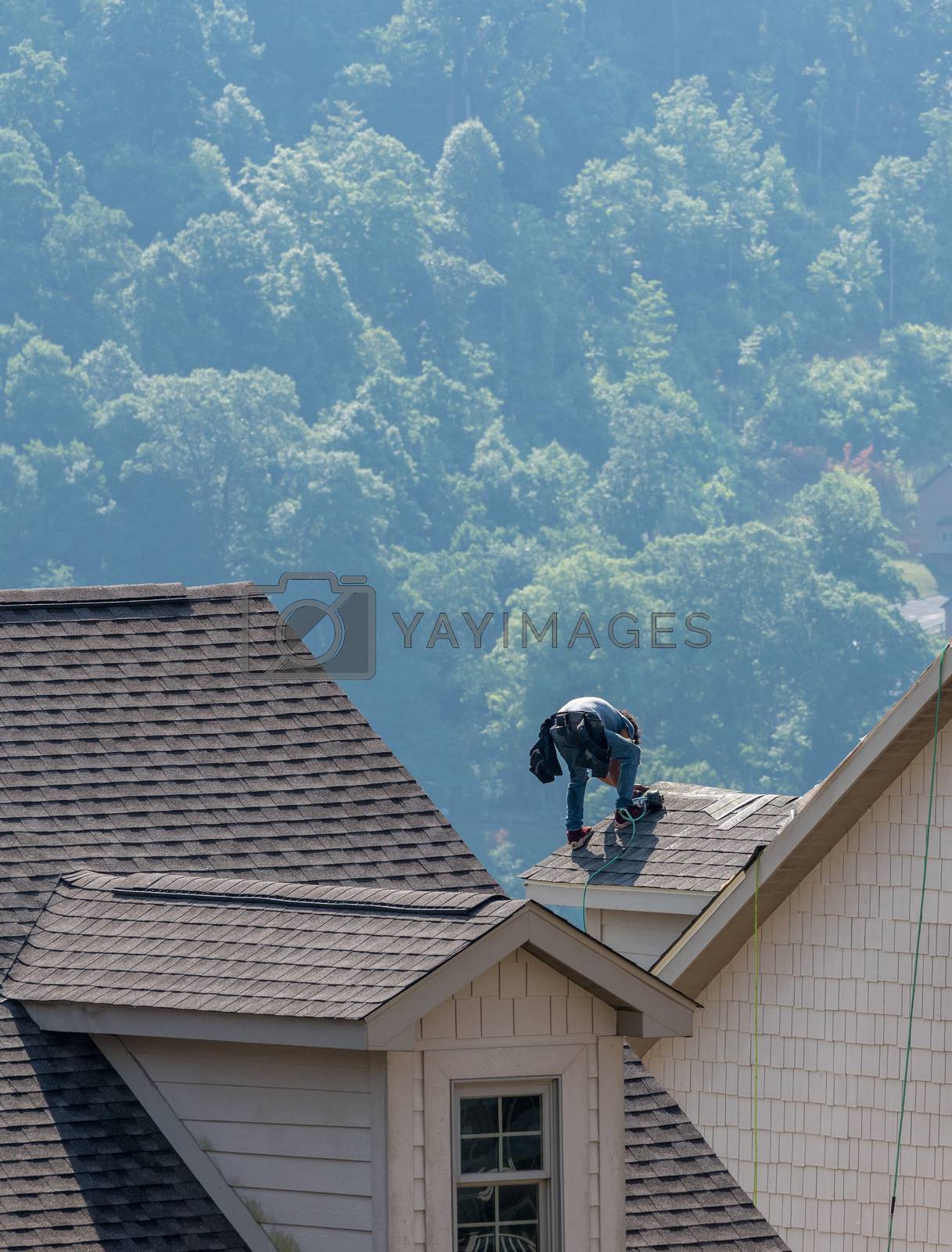 Royalty free image of Young roofing contractor nailing shingles on a roof high above the ground by steheap