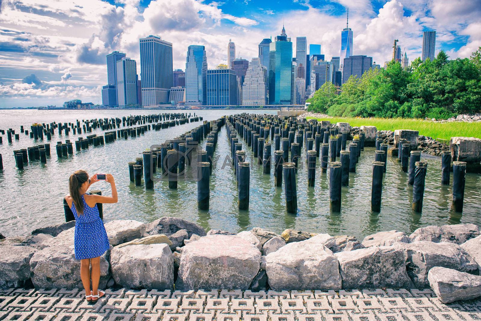 Royalty free image of New York tourist woman taking mobile picture with smartphone. Manhattan city skyline waterfront lifestyle. People walking enjoying view of downtown from the Brooklyn bridge park Pier 1 salt marsh by Maridav