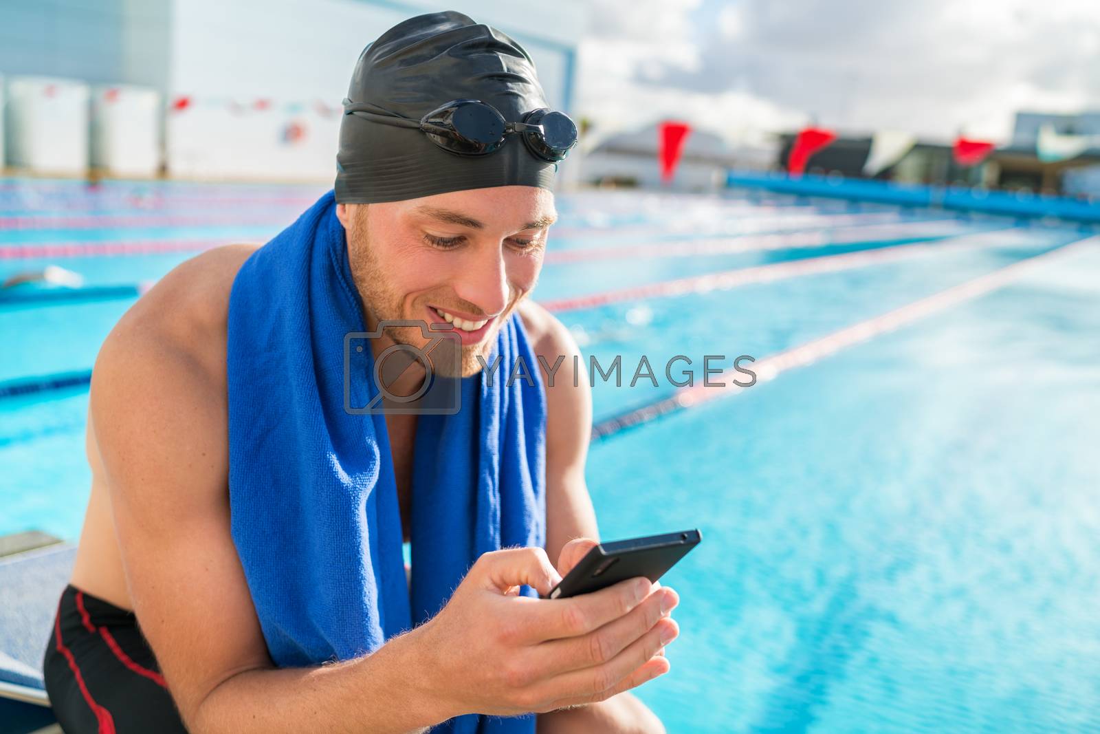 Royalty free image of Swimmer man with swimming cap and goggles at pool using his mobile phone texting on smartphone app after training in outdoor pool. Happy athlete holding cellphone at fitness centre by Maridav