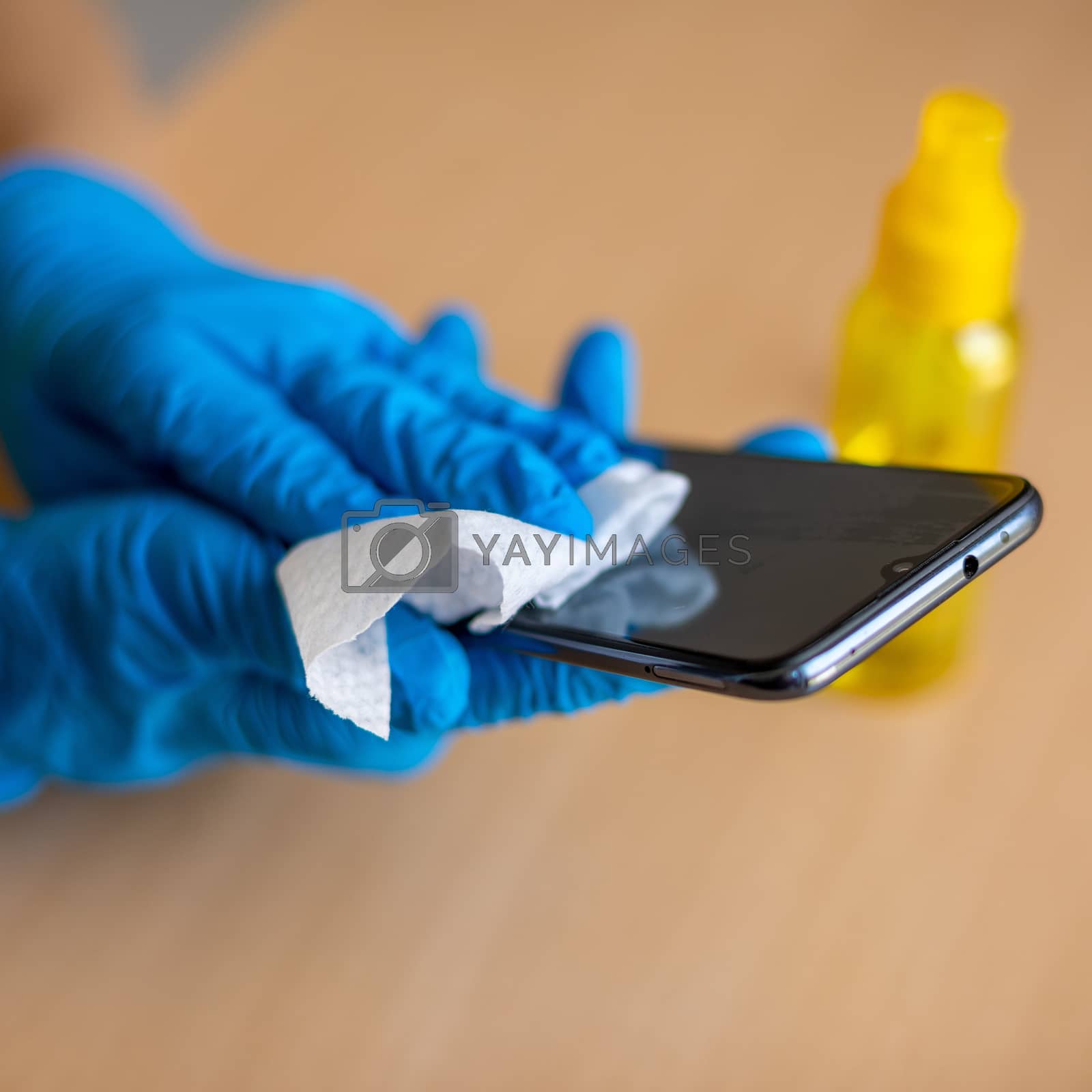 Royalty free image of Woman's hand in blue gloves sanitizing cleaning smartphone mobil by adamr