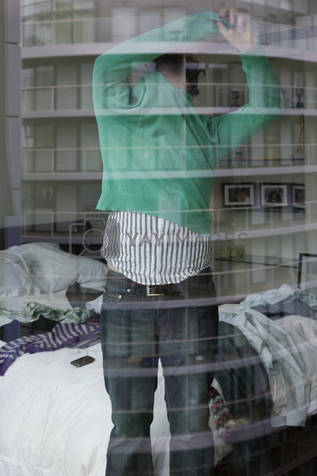 Royalty free image of Man undressing in bedroom view through window by moodboard