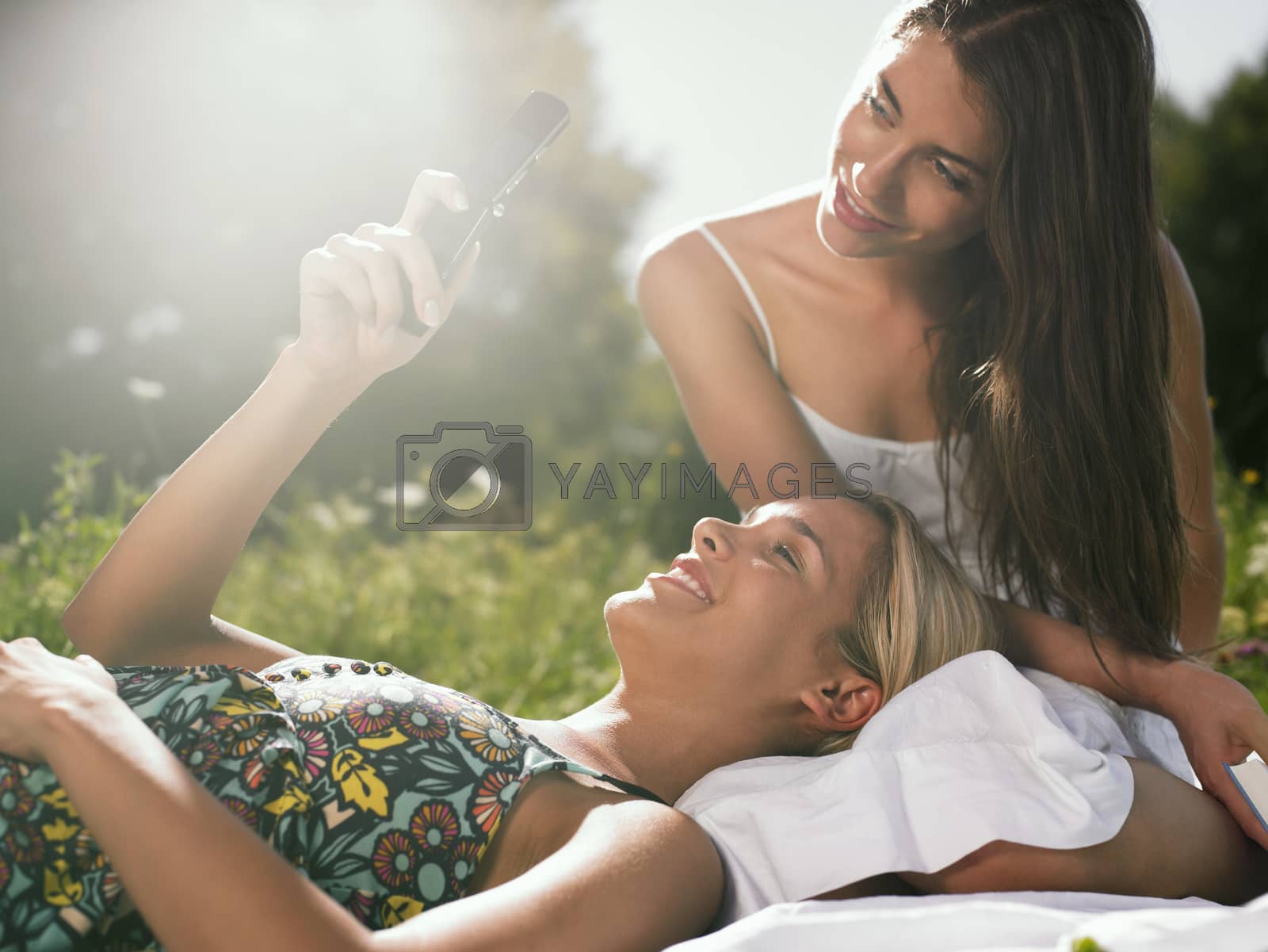 Royalty free image of Two women sitting in meadow using mobile phone by moodboard