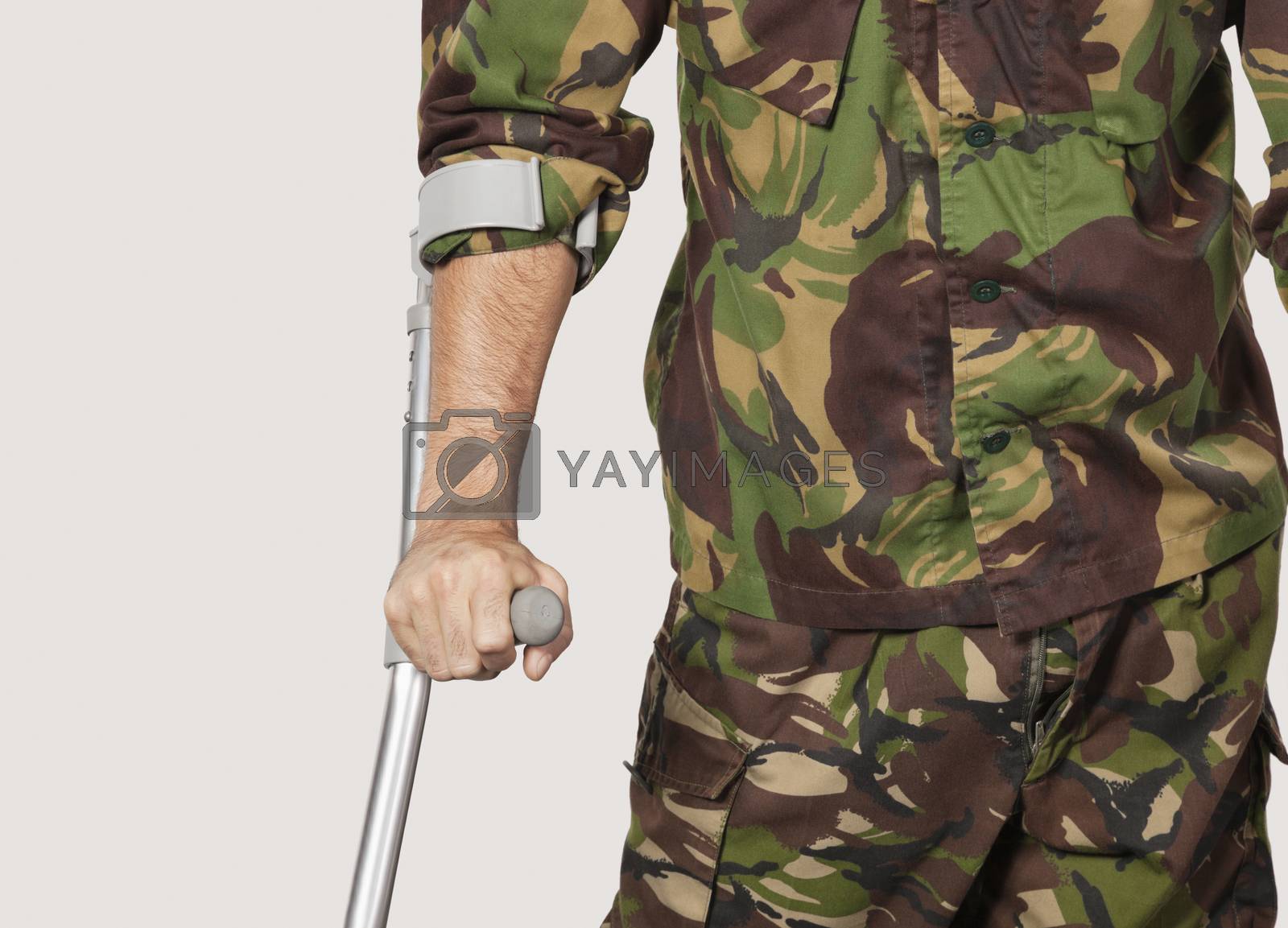 Royalty free image of Mid section of young soldier holding crutches against gray background by moodboard