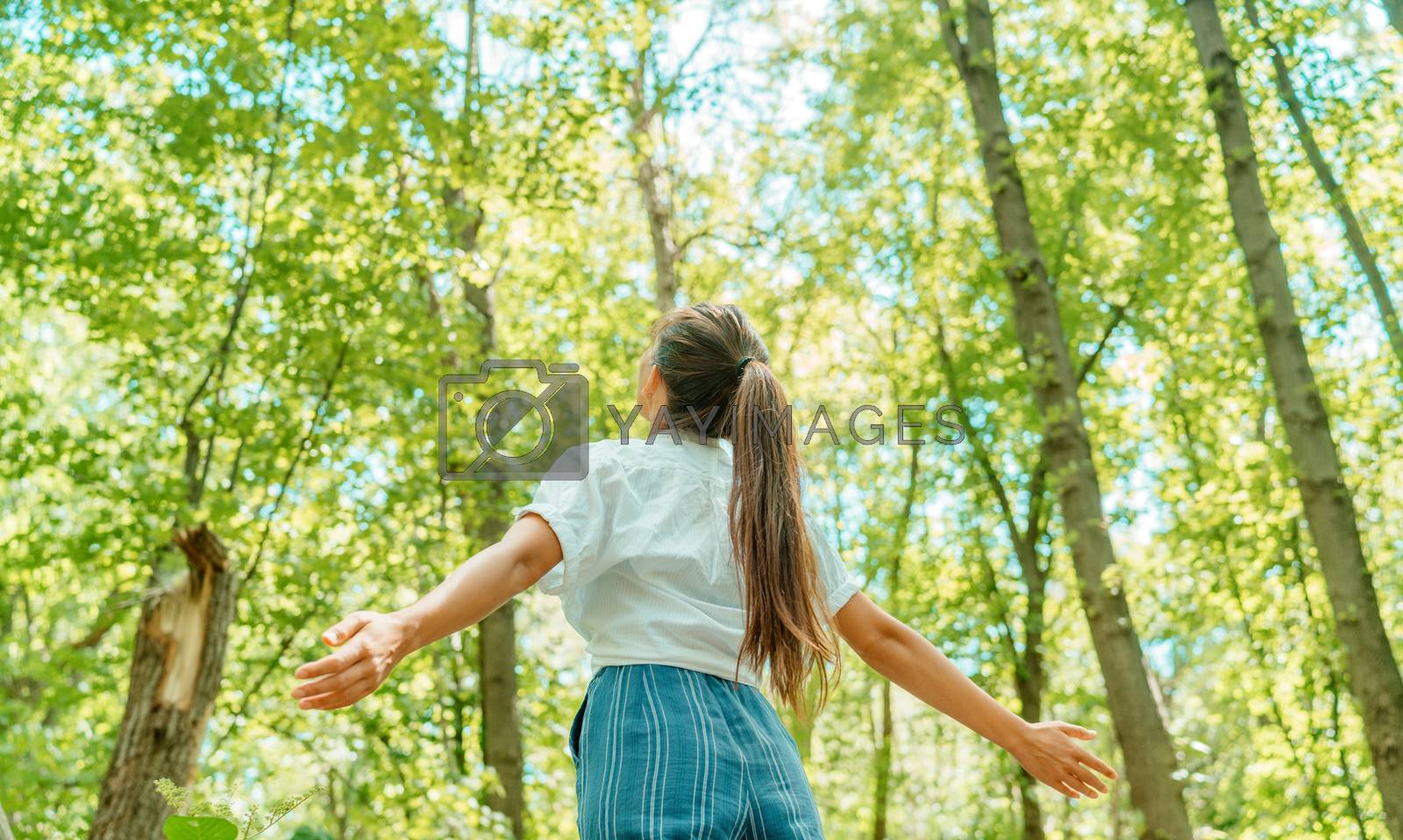 Royalty free image of Free woman breathing clean air in nature forest. Happy girl from the back with open arms in happiness. Fresh outdoor woods, wellness healthy lifestyle concept by Maridav