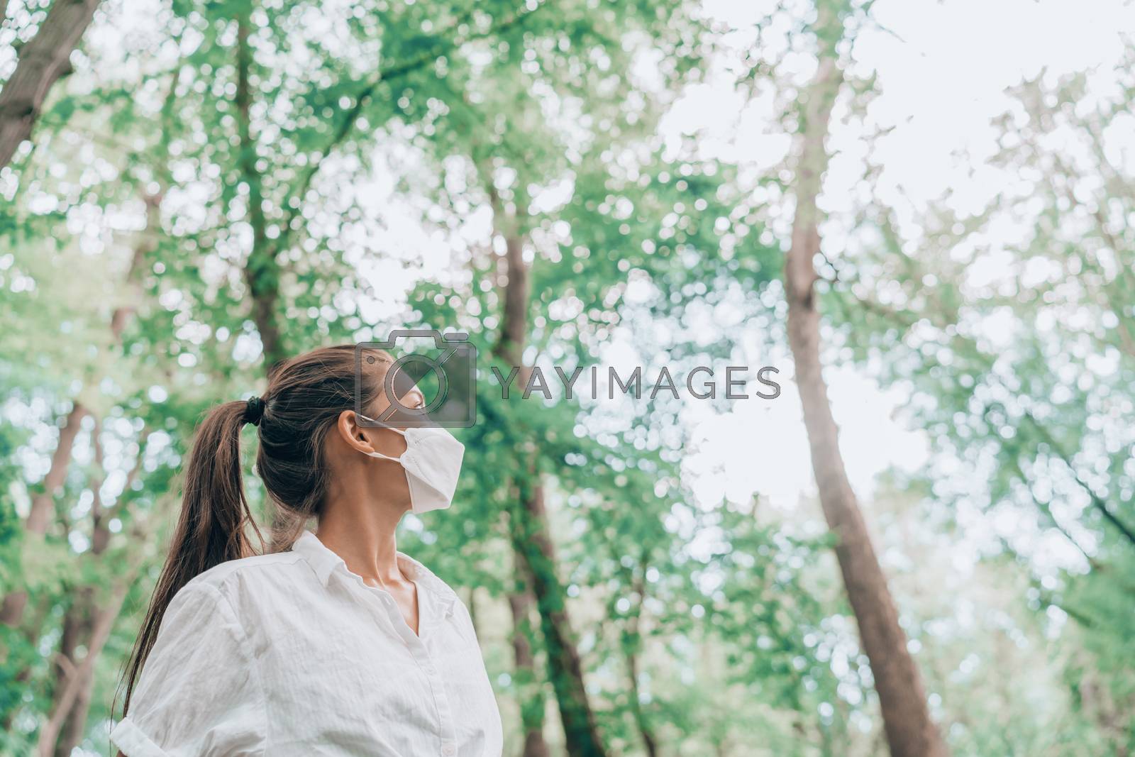 Royalty free image of Woman hiking in forest nature wearing face mask while walking outdoors, looking up at trees in hope. Clean air, sustainability, eco-friendly masks for coronavirus protection concept by Maridav