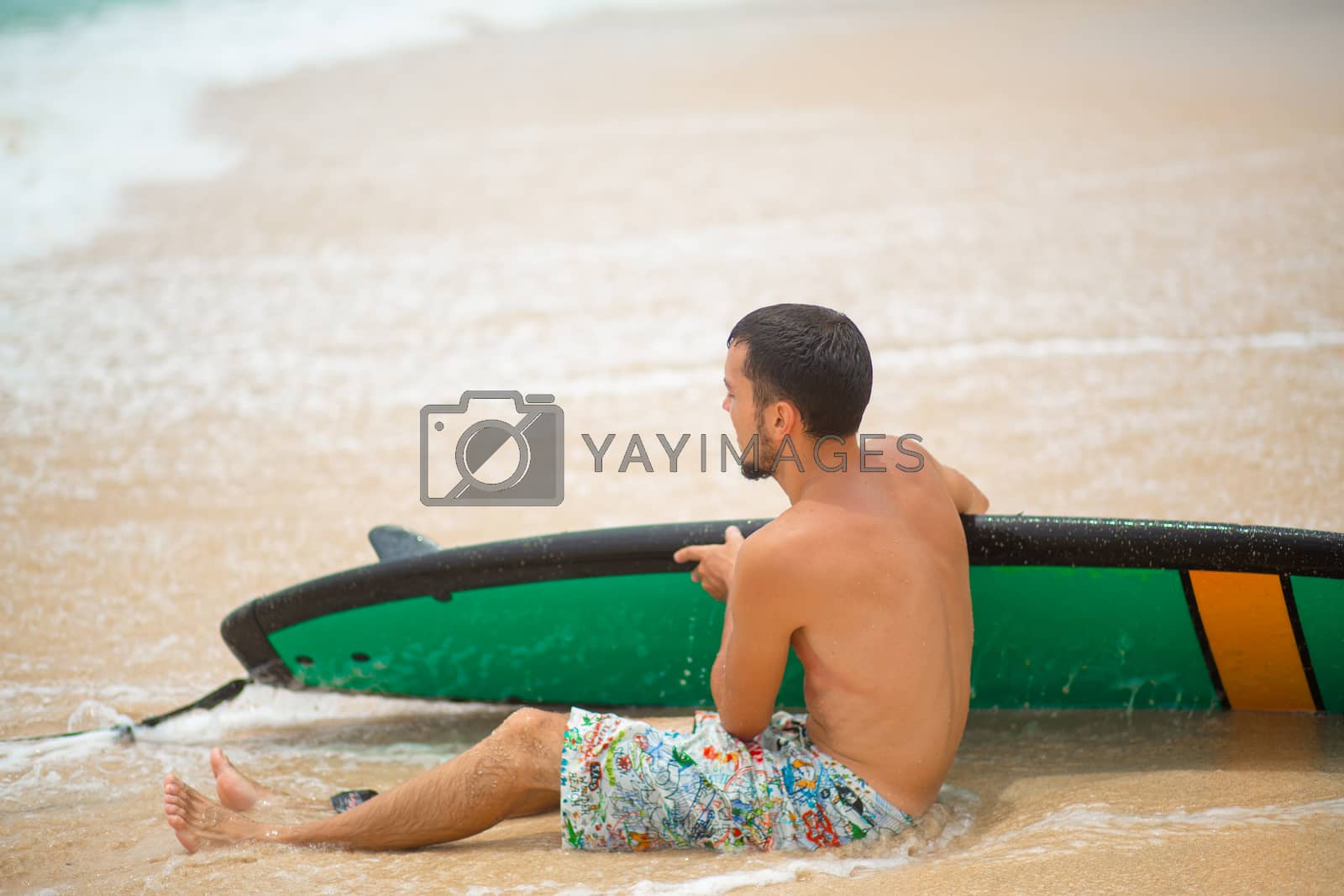 Royalty free image of The guy is resting on a sandy tropical beach, after riding a surf. Healthy active lifestyle in summer vocation by Try_my_best