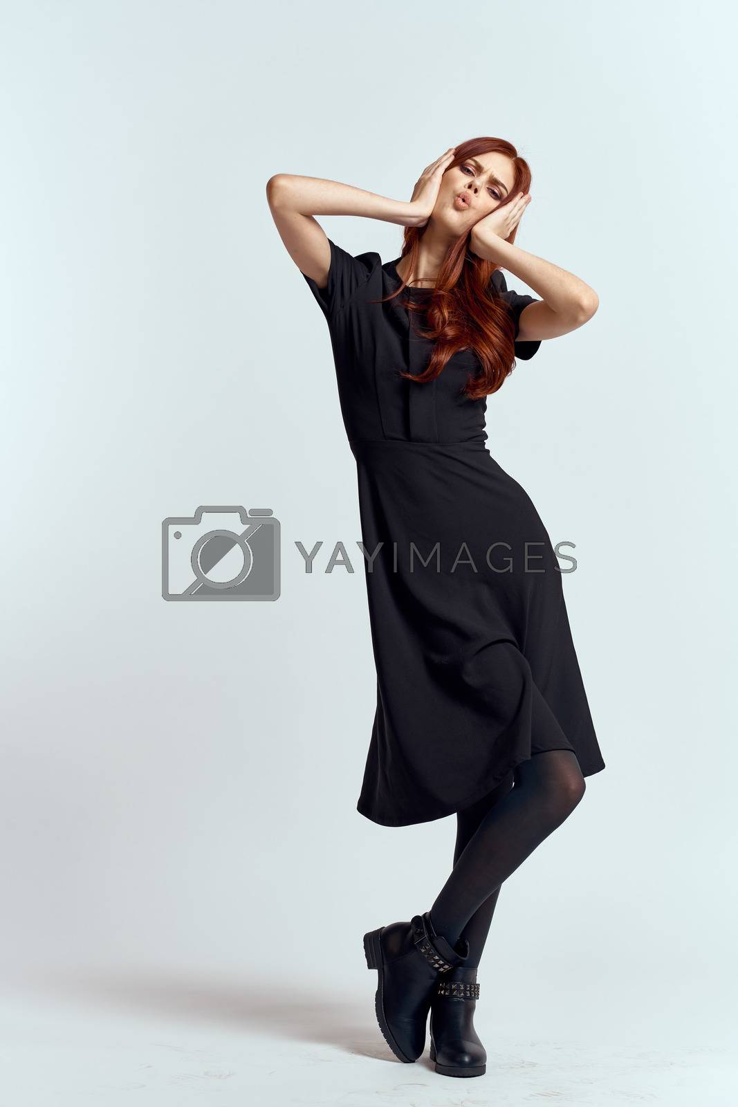Royalty free image of A woman in a black dress on a light background and pantyhose shoes red hair and pose in full growth by SHOTPRIME