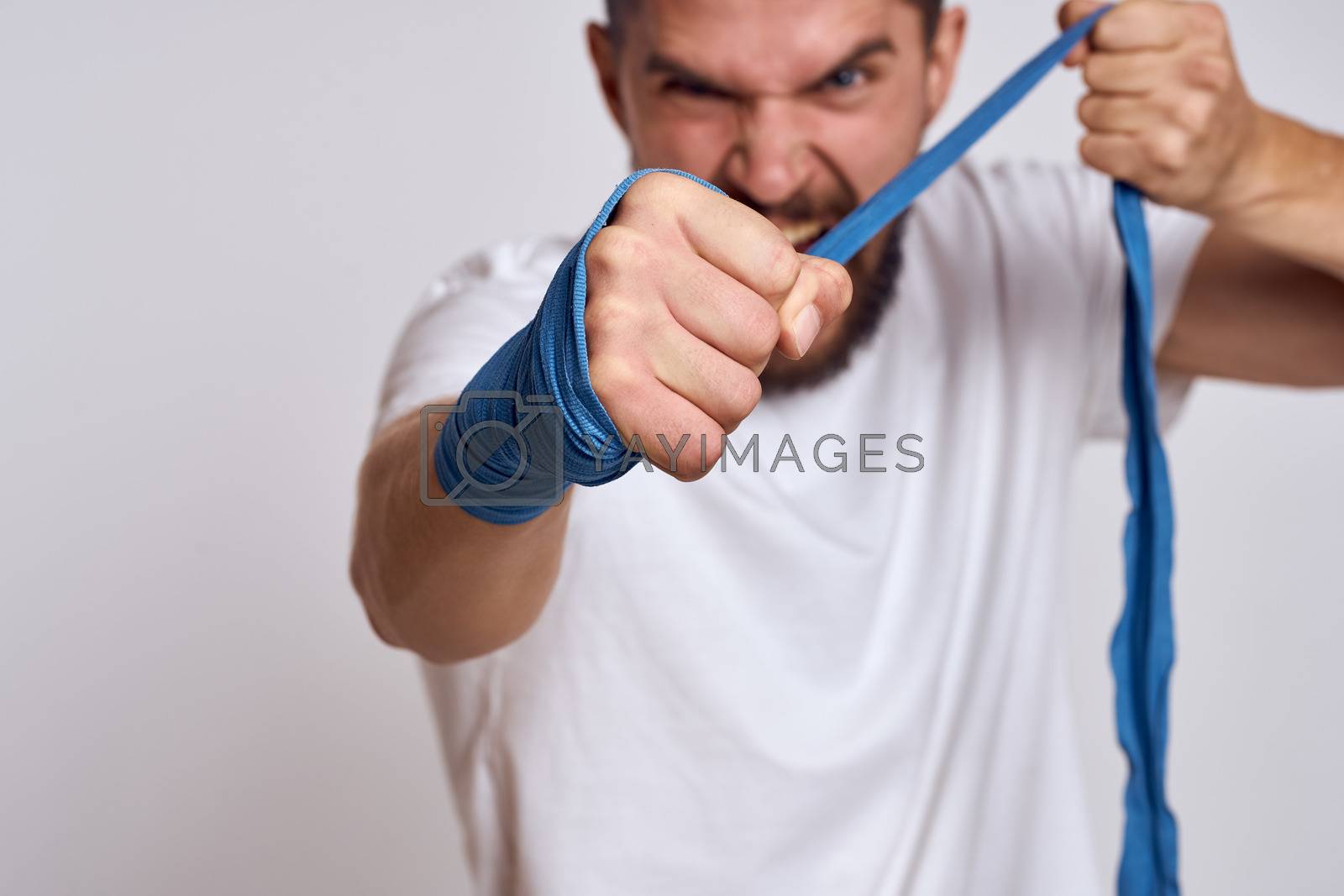 Royalty free image of A sportive man in a white T-shirt boxing bandages on his hands practicing blow exercises improving skills by SHOTPRIME
