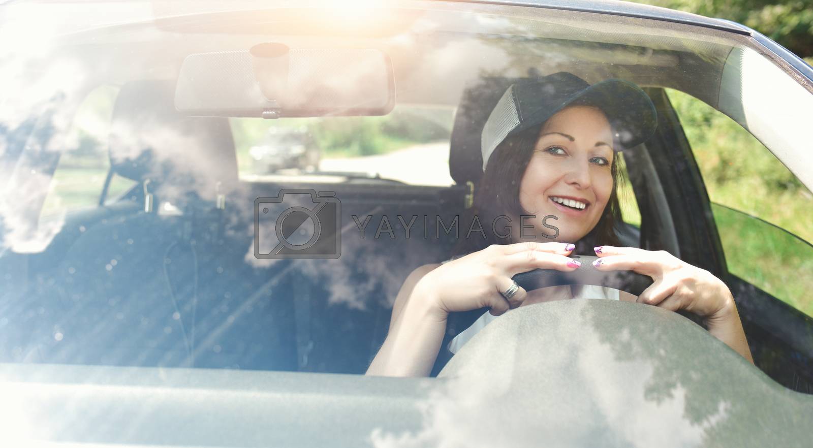 Royalty free image of Beautiful adult happy woman wearing hat driving her car in summer day by Nickstock