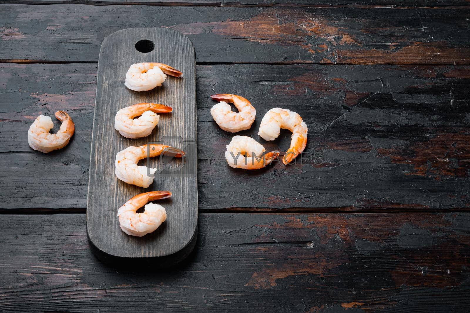 Royalty free image of Boiled peeled king prawns, on wooden cutting board, on old dark wooden table background , with copyspace and space for text by Ilianesolenyi