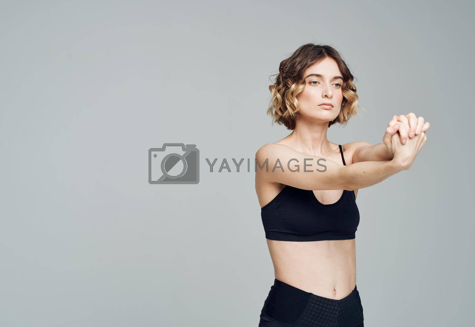 A woman in a short T-shirt on a gray background gestures with her hands to her bare shoulders Fitness Yoga asana. High quality photo