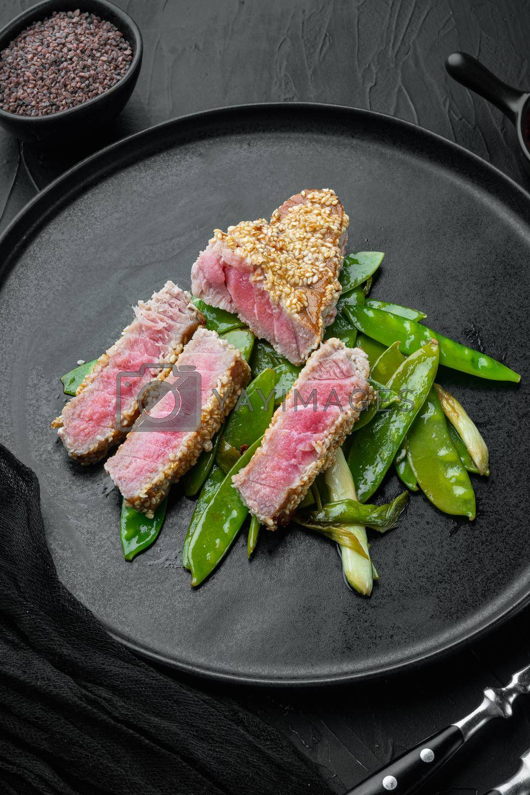 Royalty free image of Tuna steak grilled with spring onions and sugar snap peas , on plate, on black stone background by Ilianesolenyi