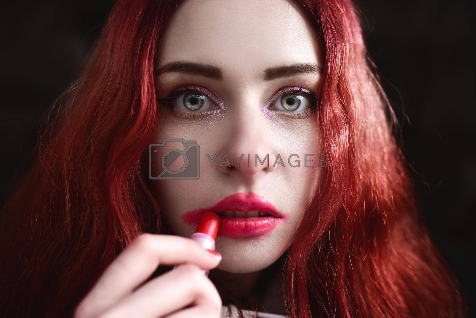 Royalty free image of Headshot of beautiful woman with nice make-up smearing red lipstick on her face, black background by Nickstock